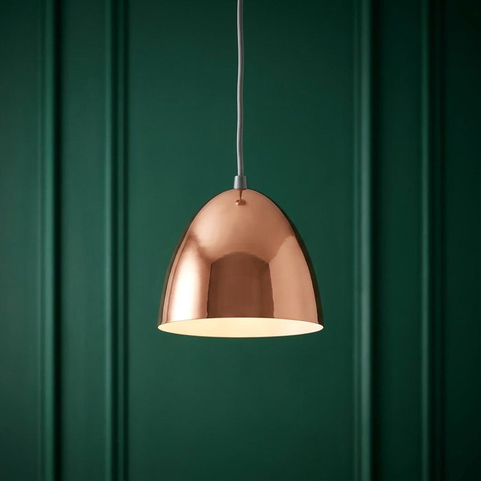 Polished copper dome pendant light with warm internal glow against a dark green wood-paneled wall.