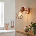 Industrial copper caged wall spotlight with a warm bulb mounted on a neutral wall above a wooden shelf.