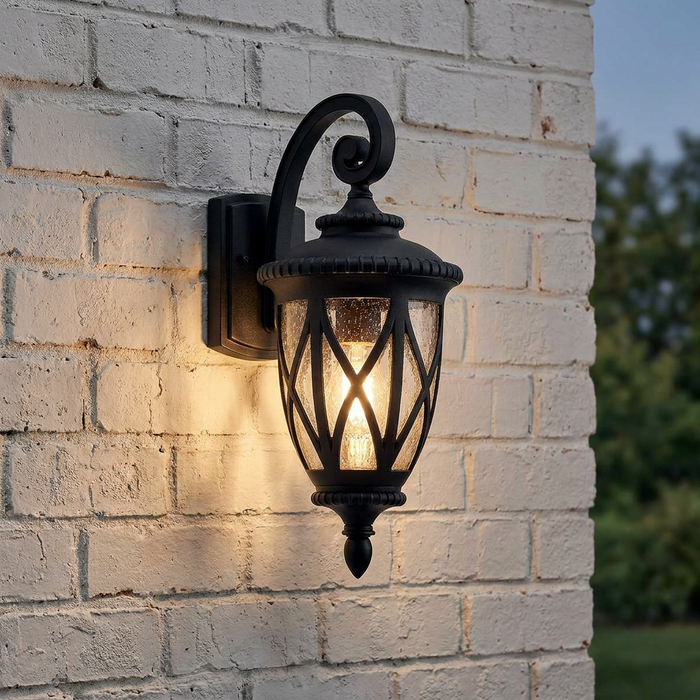 Kichler Admirals Cove black outdoor wall light with seeded glass and lantern design on a white brick wall.