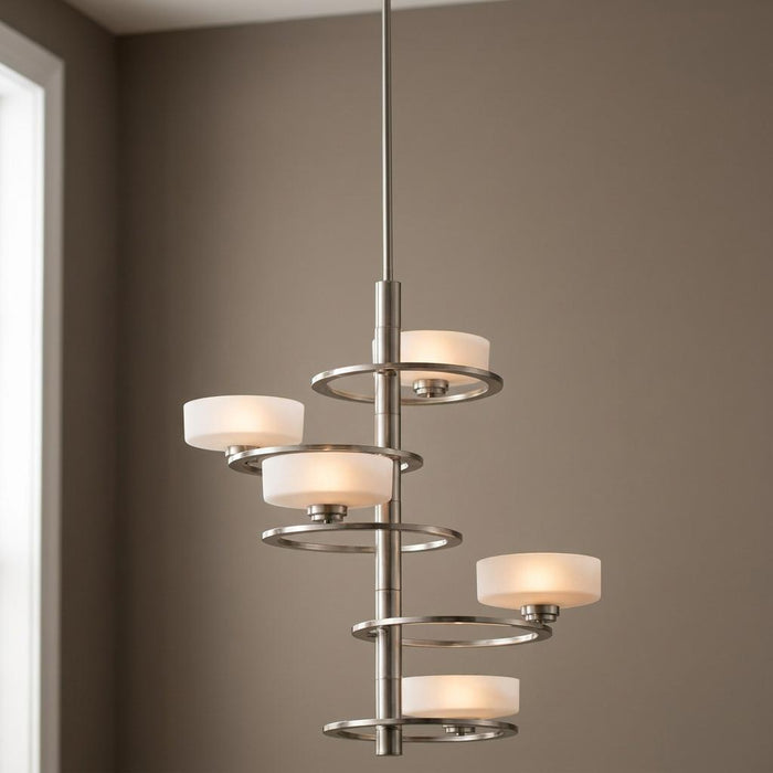A Kichler Aleeka 5-light pewter chandelier with lit white shades and metal rings against a neutral wall.