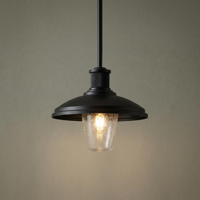 Kichler Allenbury black outdoor pendant light with a seeded glass shade and glowing bulb against a neutral wall.