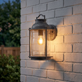 Nautical-style weathered zinc lantern with seeded glass glowing warmly on a white-painted brick exterior wall.