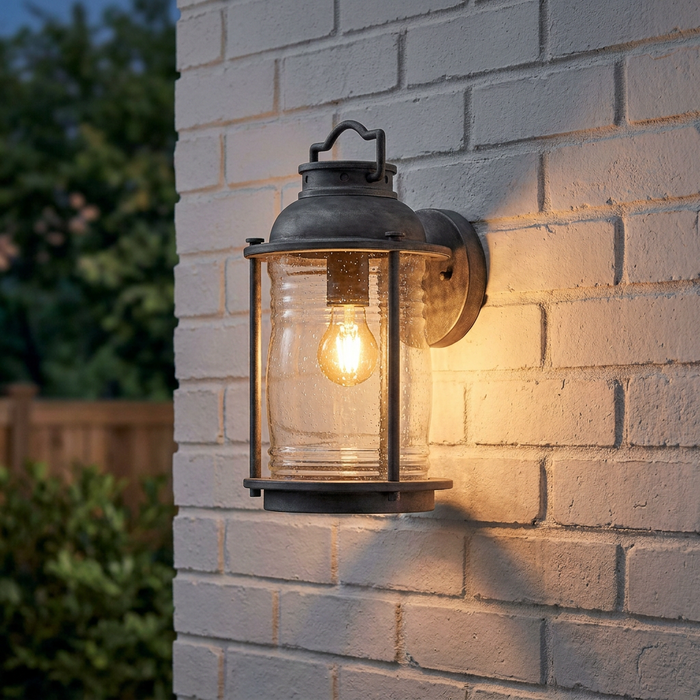 Nautical-style weathered zinc lantern with seeded glass glowing warmly on a white-painted brick exterior wall.
