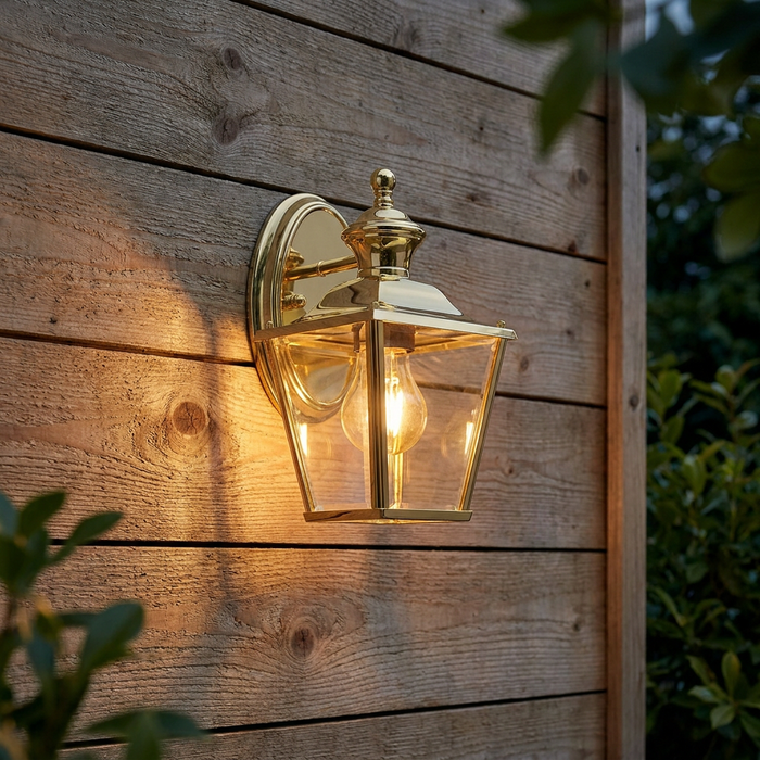 Polished brass outdoor lantern casting a warm glow on a rustic wooden wall.