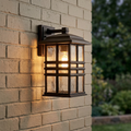 Kichler Beacon Square medium bronze outdoor lantern with rippled glass glowing on a light-colored brick wall.