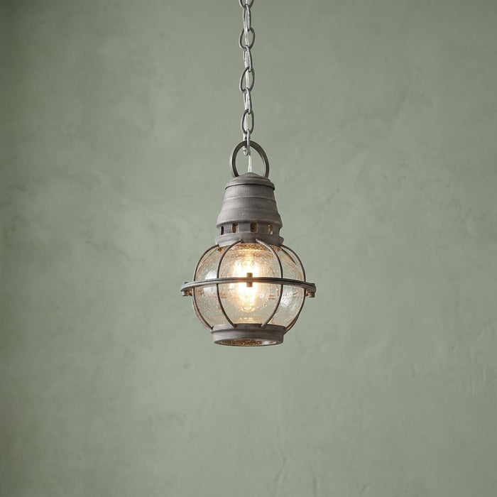 Nautical weathered zinc pendant light with a seeded glass globe hanging against a textured sage green wall.