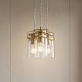 Kichler Brindley 3-light brass pendant with clear glass cylinder shades hanging in a cluster against a neutral wall.