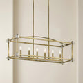 A linear brass chandelier with six candle bulbs and clear crystal corner accents hangs against a cream background.