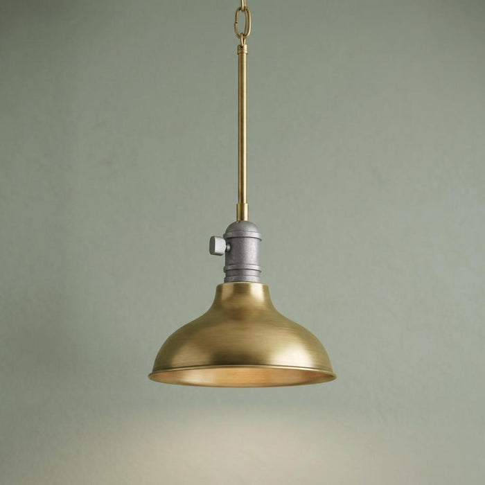 Industrial mini pendant with natural brass dome shade and grey metal socket against a sage green background.