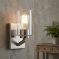 Silver wall light with a seeded glass shade and wooden arm, mounted on a textured gray wall.