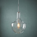 Chrome pendant light with a clear glass shade and warm Edison bulb against a textured teal wall.