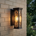 Kichler Franceasi bronze outdoor wall light with decorative scrollwork mounted on a light brick wall, glowing warm light.