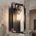 Industrial wall light with a black and brass pipe frame and exposed Edison bulb on a distressed concrete wall.