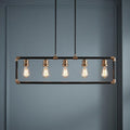 Industrial five-light linear chandelier with a black and brass frame and Edison bulbs against a blue wall.