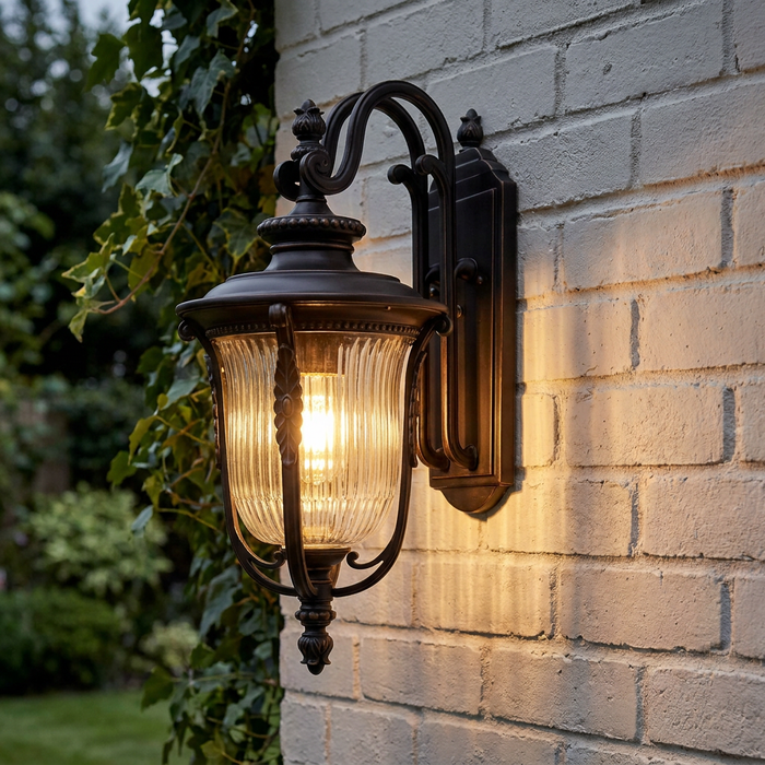Kichler Luverne rubbed bronze outdoor wall lantern with ribbed glass glowing on a white brick wall.