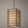 Large bronze pendant light with a fabric shade encased in a curved horizontal slat metal frame.