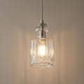Brushed nickel pendant light with a clear ribbed glass cylinder shade casting a warm glow against a neutral wall.