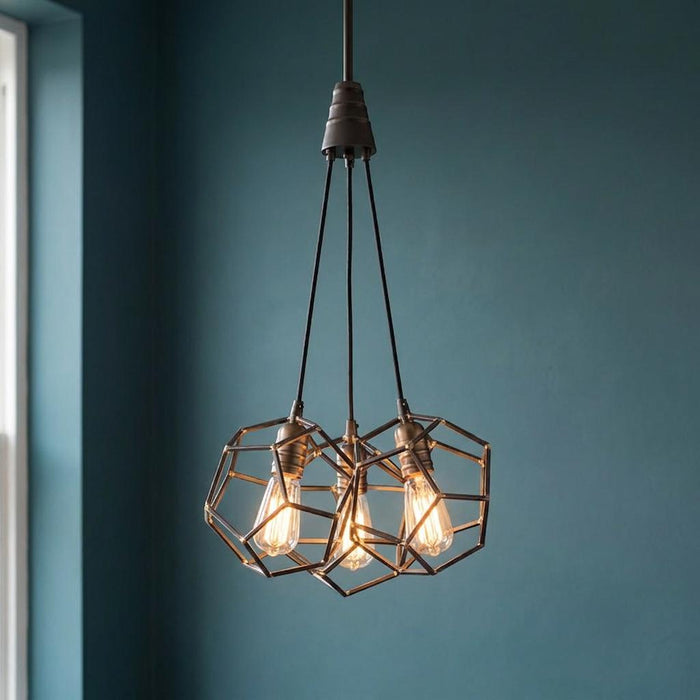Kichler Rocklyn 3 light chandelier featuring raw steel geometric cages and warm Edison bulbs against a teal wall.
