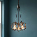 Kichler Rocklyn 3 light chandelier featuring raw steel geometric cages and warm Edison bulbs against a teal wall.