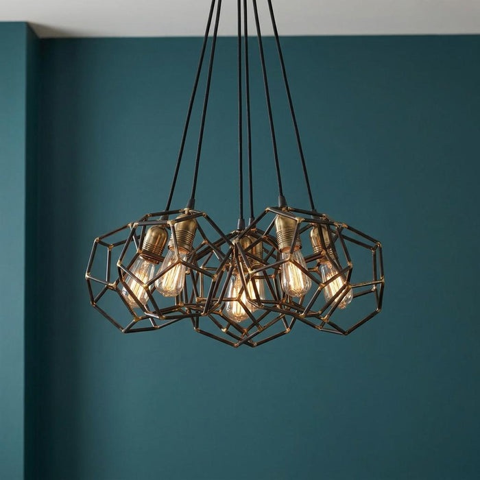 Industrial 6-light chandelier with raw steel geometric cages and brass accents hanging against a teal wall.