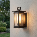 Bronze lantern outdoor wall light with an illuminated frosted glass cylinder on a textured white wall.