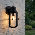 Black nautical outdoor wall light with seeded glass and a glowing bulb, mounted on a white brick wall.
