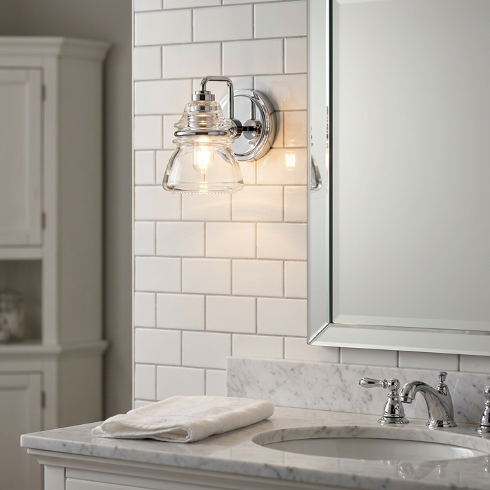 Chrome wall light with clear glass shade mounted on white subway tiles above a bathroom vanity.