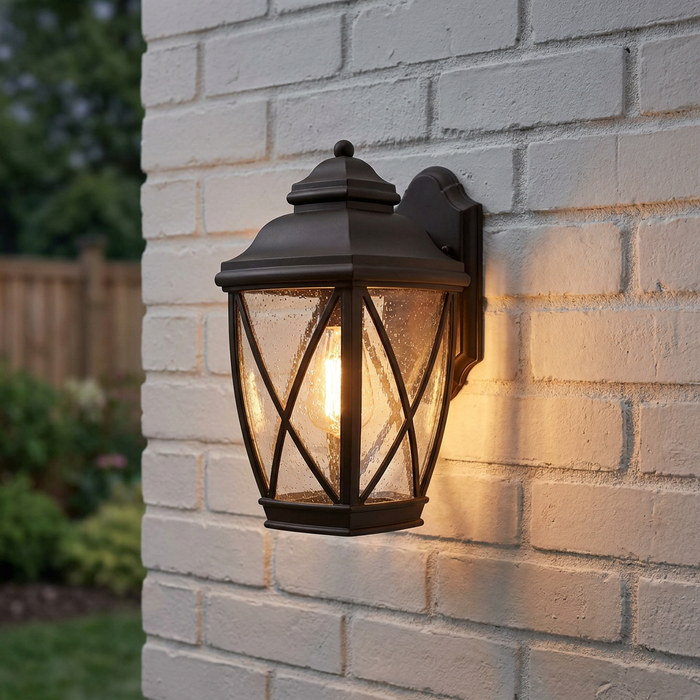 Illuminated bronze lantern-style outdoor light with seeded glass mounted on a white brick wall.