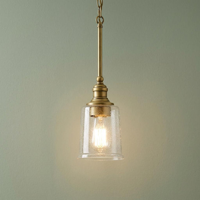 Brass mini ceiling pendant with a seeded glass shade and lit bulb hanging against a green wall.