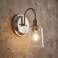 Pewter wall sconce with a curved arm and seeded glass shade, glowing against a textured beige wall.