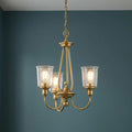 Three-light natural brass chandelier with clear seeded glass shades against a teal wall.