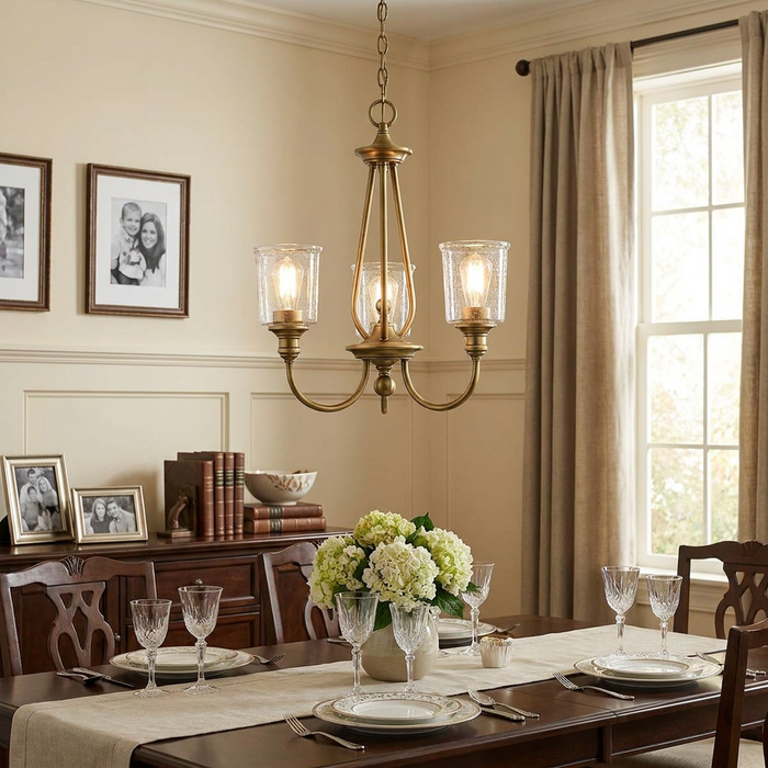 A Kichler Waverly 3-light natural brass chandelier with seeded glass shades hanging above a dining room table.