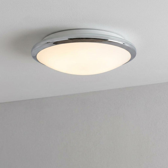 Circular flush mount bathroom ceiling light with a polished chrome rim and a glowing frosted glass diffuser.