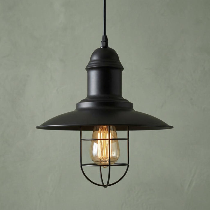 Industrial black ceiling pendant light with a metal cage and glowing filament bulb against a green wall.