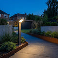 Sleek grey LED bollard post lighting a modern stone garden path at twilight.
