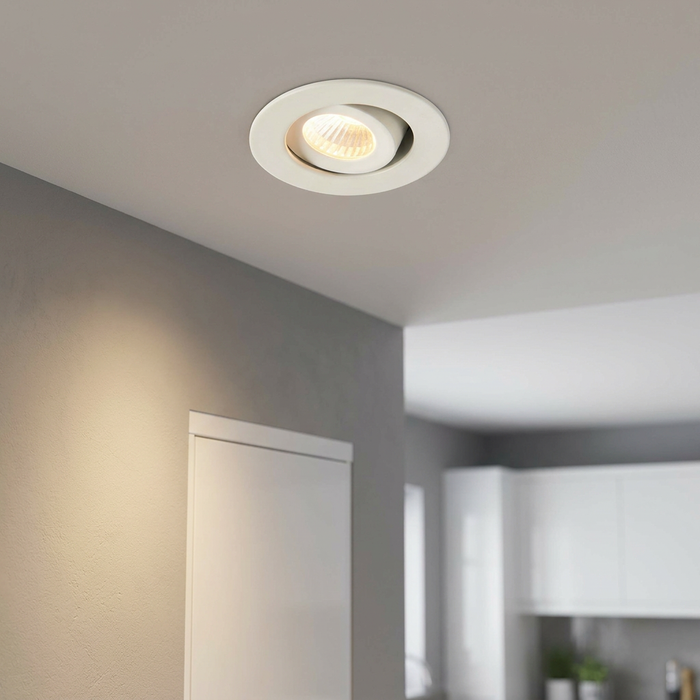 A white circular recessed LED spotlight tilted to cast a warm glow on a wall in a modern room.