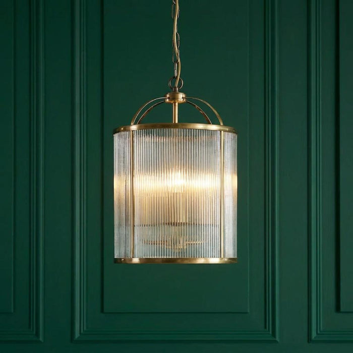 Lambeth 4 Light Brass & Ribbed Glass Ceiling Pendant glowing against a dark green paneled wall.