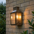 Brass lantern outdoor wall light with an illuminated bulb mounted on a brick wall.