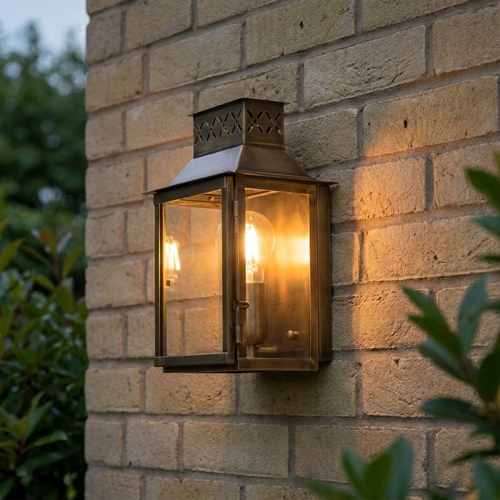 Brass lantern outdoor wall light with an illuminated bulb mounted on a brick wall.