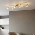 Lana 6-light polished brass ceiling light with crystal globes on a wavy bar, set in a modern neutral interior.
