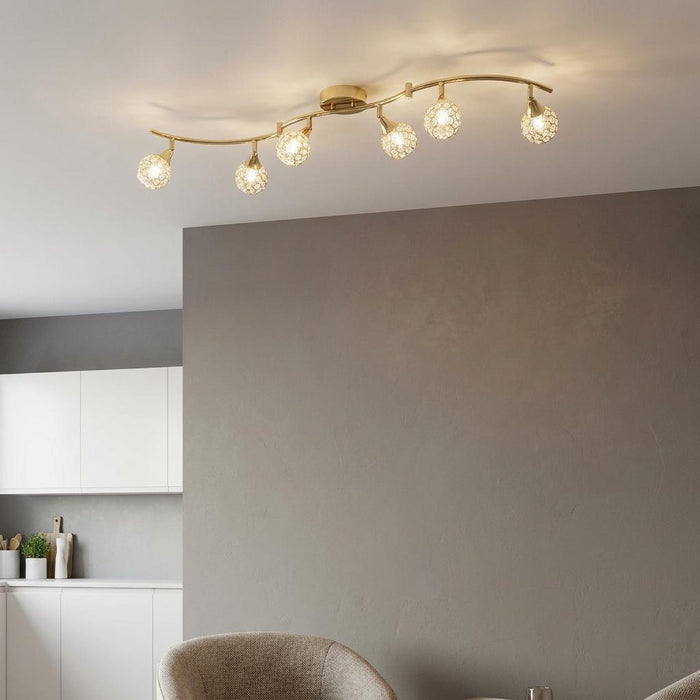 Lana 6-light polished brass ceiling light with crystal globes on a wavy bar, set in a modern neutral interior.