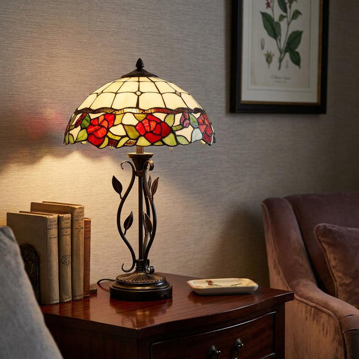 Tiffany table lamp with a red rose stained glass shade and ornate metal base on a wooden side table.