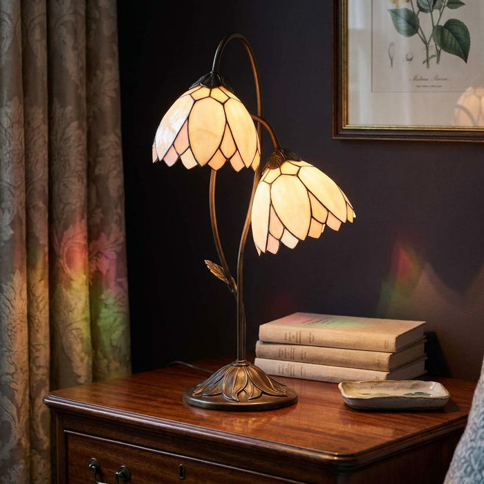 A double lily Tiffany table lamp with cream stained-glass shades on a dark wooden bedside table.