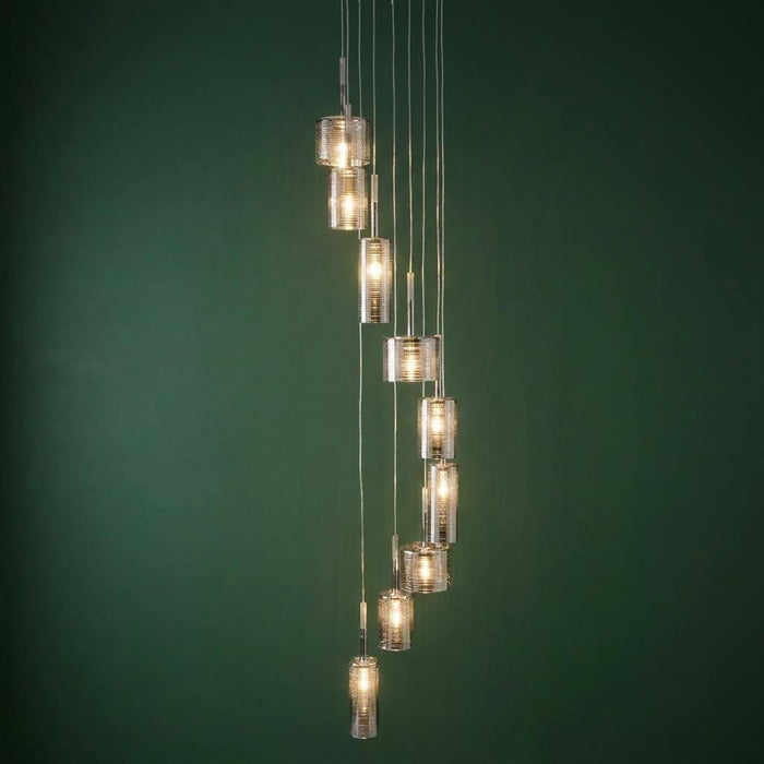 Linen 9 light multi-drop chrome pendant with cylindrical glass shades in a spiral arrangement against a green wall.