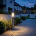 Louvred stainless steel bollard light illuminating a paved garden walkway at dusk.