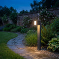 Lutec Cuba grey LED bollard light with an adjustable head illuminating a garden path at dusk.