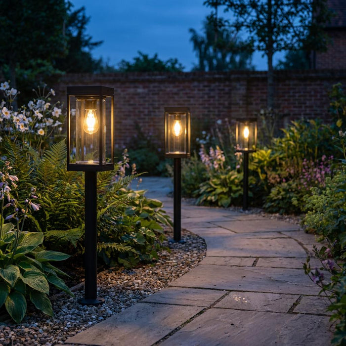 Three black solar bollard lights illuminating a winding stone garden path at dusk.