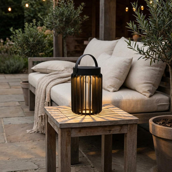 A black slatted solar lantern glows on a wooden side table in a cozy outdoor patio setting.
