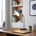 Dark grey Madison desk lamp with a chrome neck illuminating a wooden desk with a laptop and books.