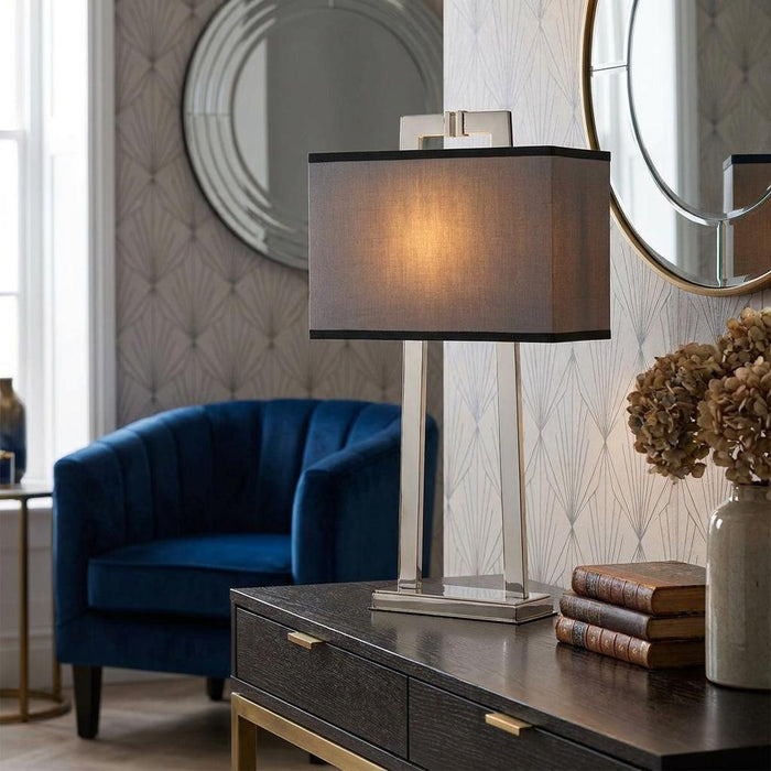 Magro polished nickel table lamp with a grey rectangular shade on a dark wooden console table.
